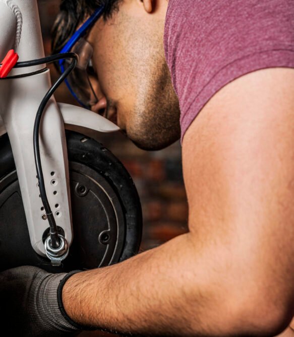 A mechanic with safety glasses installing the new or repaired wheel on an electric scooter A latin mechanic with safety glasses installing the new or repaired wheel on an electric scooter in his workshop